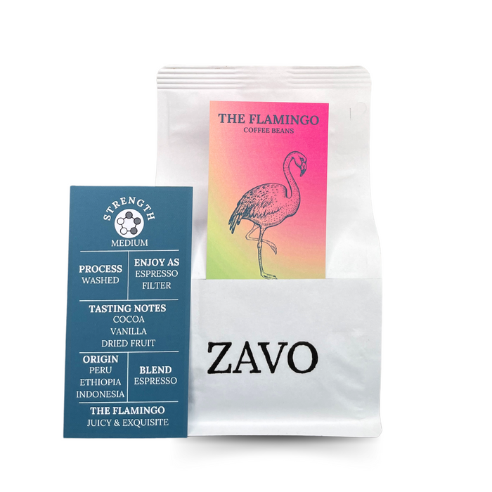 A white coffee bag with a black ZAVO logo stamped on the bottom of the bag, there is two product cards one is pink and yellow with a Flamingo on, the second is the tasting notes which says Strength Medium, Process Washed, Enjoy as Espresso, Filter, Tasting Notes Cocoa Vanilla Dried Fruit, Origin Peru Ethiopia, Indonesia, Blend Espresso, The Flamingo Juicy & Exquisite