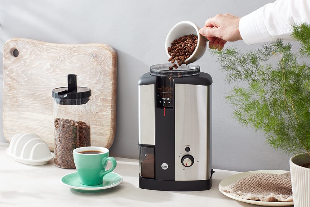 Beans going in to the Svart Coffee Grinder machine, there is a green cup of coffee next to it and a glass jar of beans.