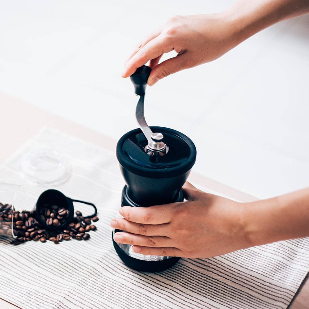 A Hario Ceramic Grinder in action, it is a staged shot with coffee beans placed by the side of the grinder.