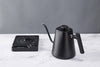 A black Felicita temperature control electric kettle  on a marble background with the stand in the background